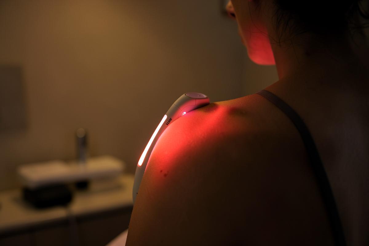 Aplicação de laser terapêutico com luz vermelha sobre o ombro de uma pessoa